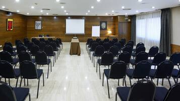 Un salón de conferencias con filas de sillas, un atril, una pantalla de proyector y una pizarra.