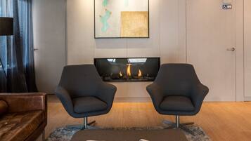 A modern hotel lobby with two armchairs, a fireplace, a mounted artwork, and a WC sign.