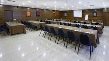 A conference room with multiple tables and chairs, equipped with water bottles and glasses, and a projector screen.