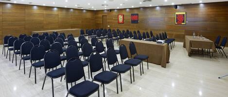 A conference room with rows of chairs, a long table, and wooden panel walls.