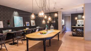 A modern dining area with a long table, multiple chairs, pendant lighting, and a decorative vase.