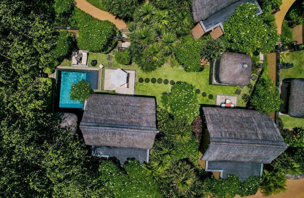 Vista aérea de un resort con varias cabañas de techo de paja, una piscina central y exuberante vegetación.