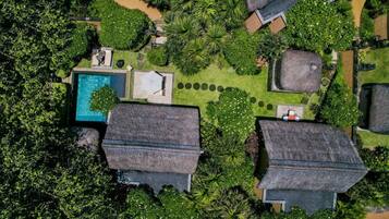 Vista aérea de un resort con varias cabañas de techo de paja, una piscina central y exuberante vegetación.