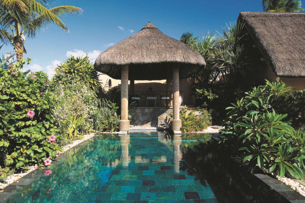 A pool area with a thatched-roof structure, surrounded by lush greenery and palm trees.