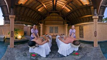A spa area with two massage tables under a thatched roof, surrounded by a pool.