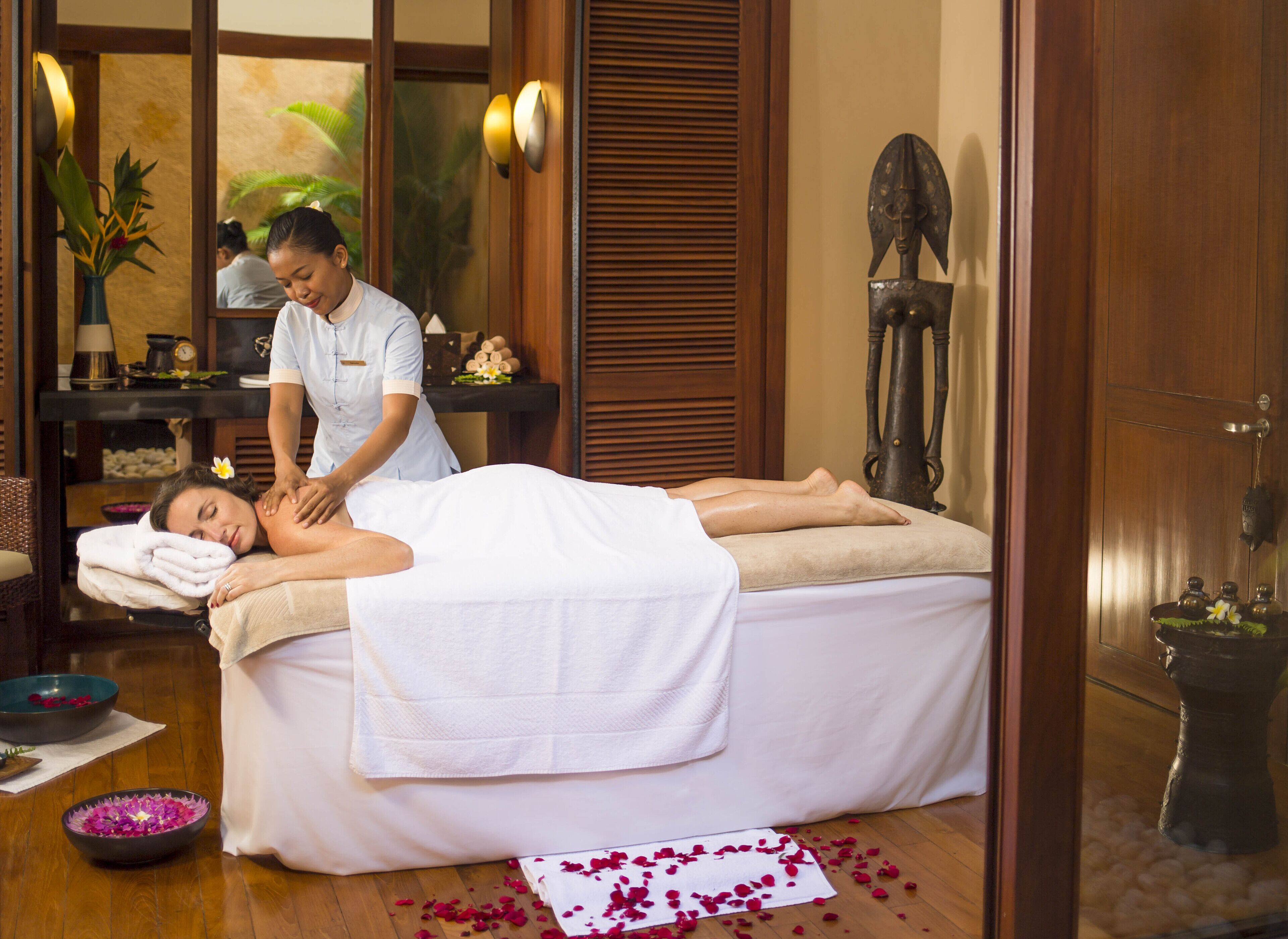 A massage room with a massage table, towels, and a decorative statue.