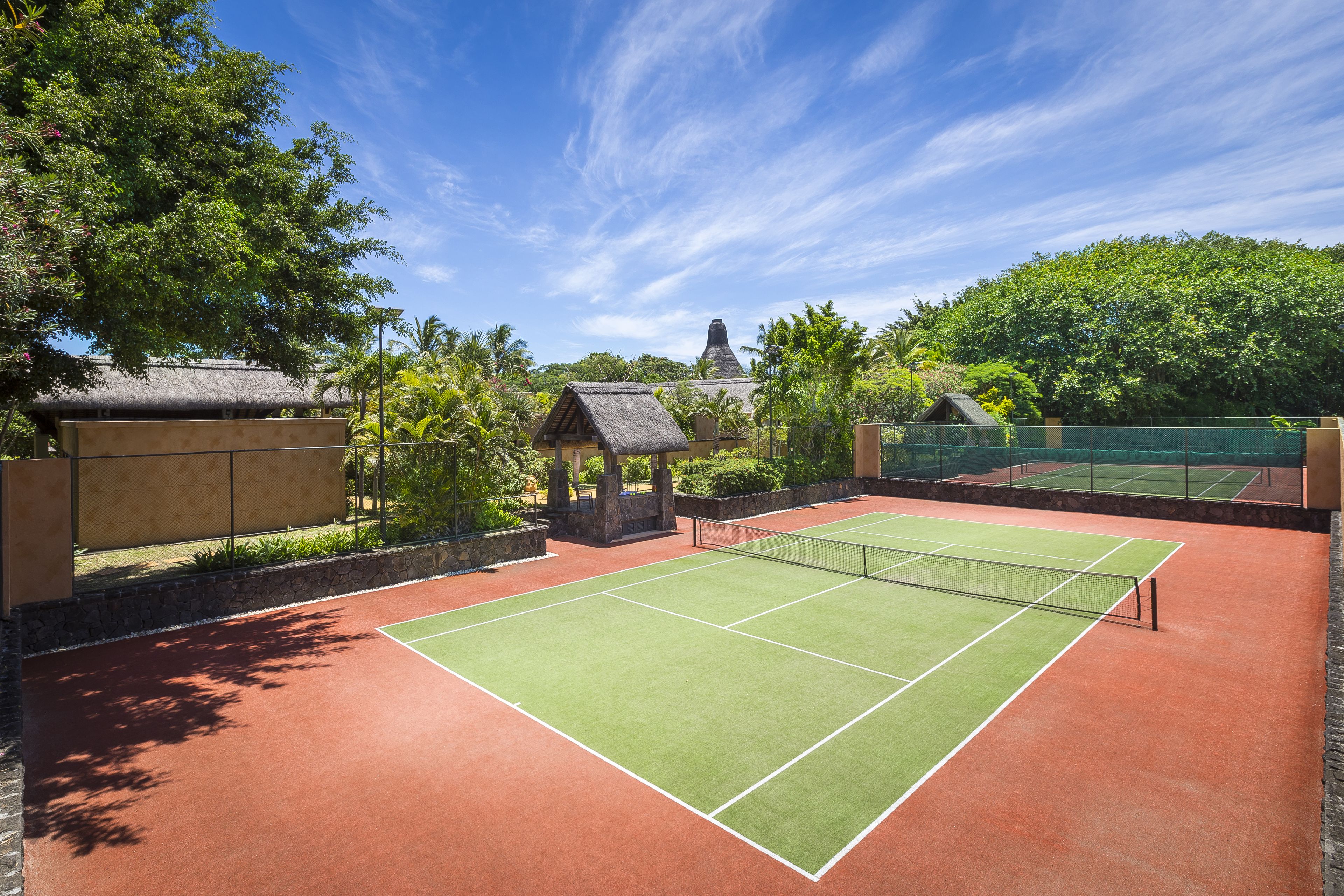 A tennis court with a net, surrounded by trees and a stone wall.