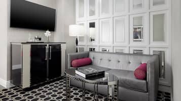 Een moderne hotelkamer met een flatscreen televisie, een minibar, een bank met decoratieve kussens en een kamer met een patroon vloer.