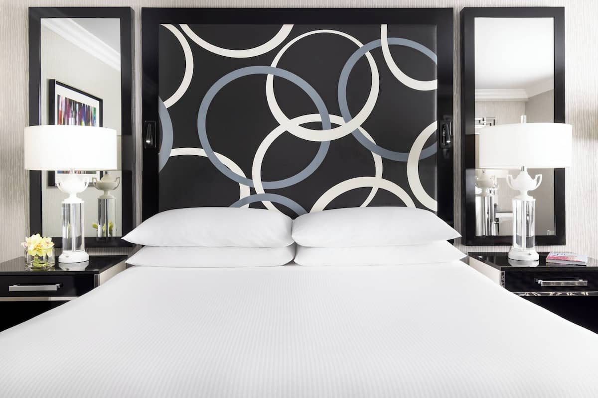 A hotel room with a large bed, two bedside tables, a modern abstract wall design, and two lamps.