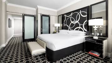 A hotel room with a large bed, a bench, a bedside table with a lamp, and a mirror.