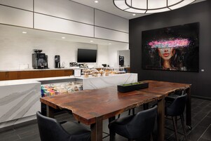 A modern kitchen with a marble countertop, coffee machines, and a large painting on the wall.