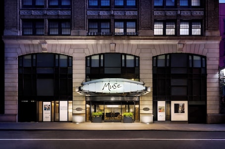 A building with a prominent 'MUSE' sign, large windows, and potted plants at the entrance.