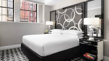 A modern hotel room with a large bed, a nightstand with a lamp, a mirror, and a view of the city through a window.