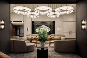 A lobby with a central floral arrangement, multiple seating areas, and a modern chandelier. - The Muse New York (New York)