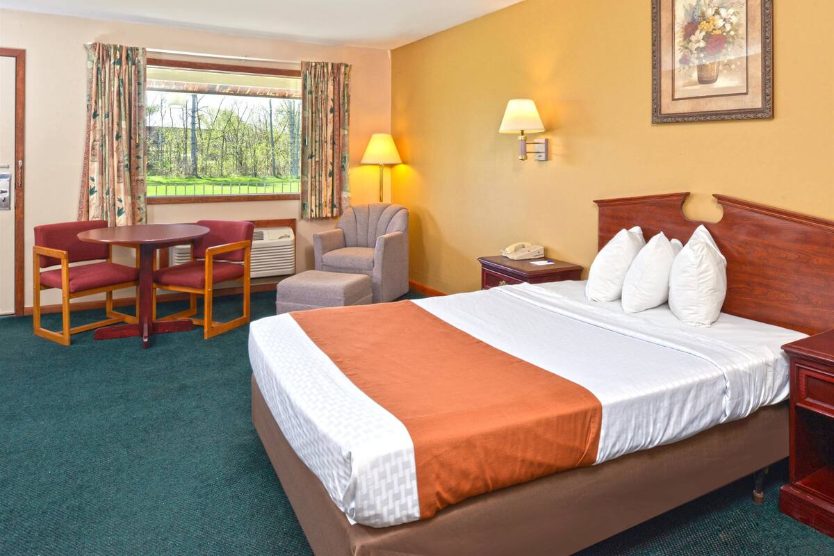 A hotel room with a large bed, a desk, two chairs, a lamp, and a nightstand.