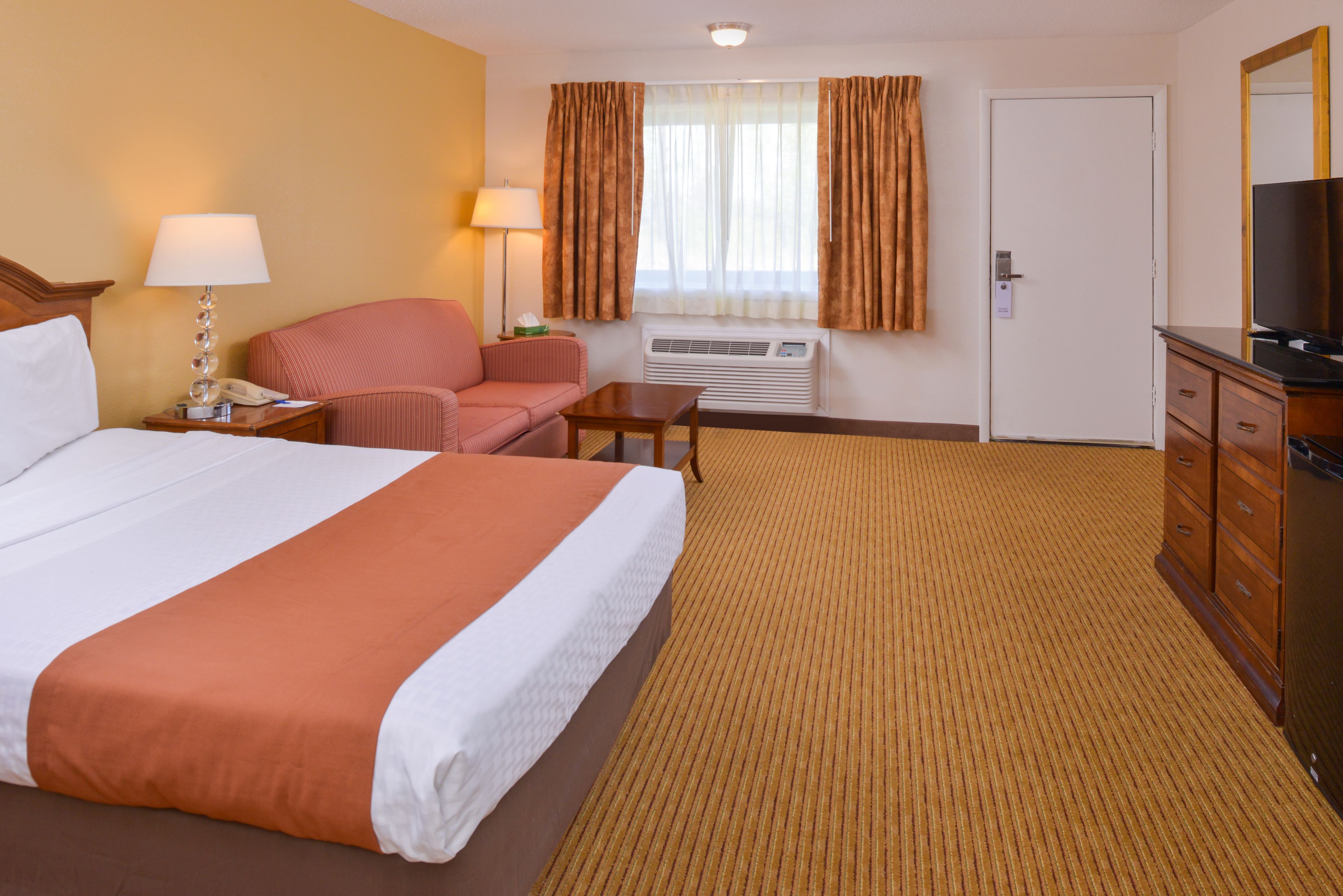 Ein Hotelzimmer mit einem großen Bett, einem Schreibtisch, einem Sessel, einem Fernseher und einer Kommode.