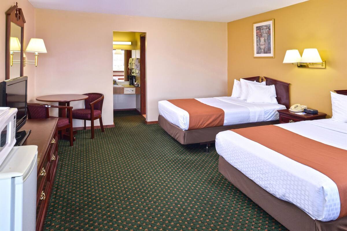 A hotel room with two beds, a desk with a chair, a television, and a bathroom visible through an open door.