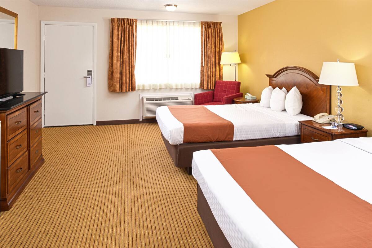 A hotel room with two beds, a television, a desk, and a chair.