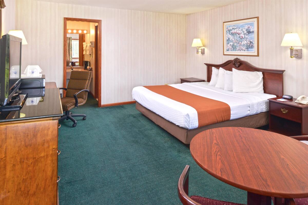 A hotel room with a large bed, a desk with a telephone, a chair, and a small table.