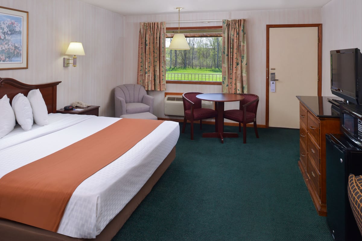 A hotel room with a large bed, a desk, a chair, a television, and a window with curtains.
