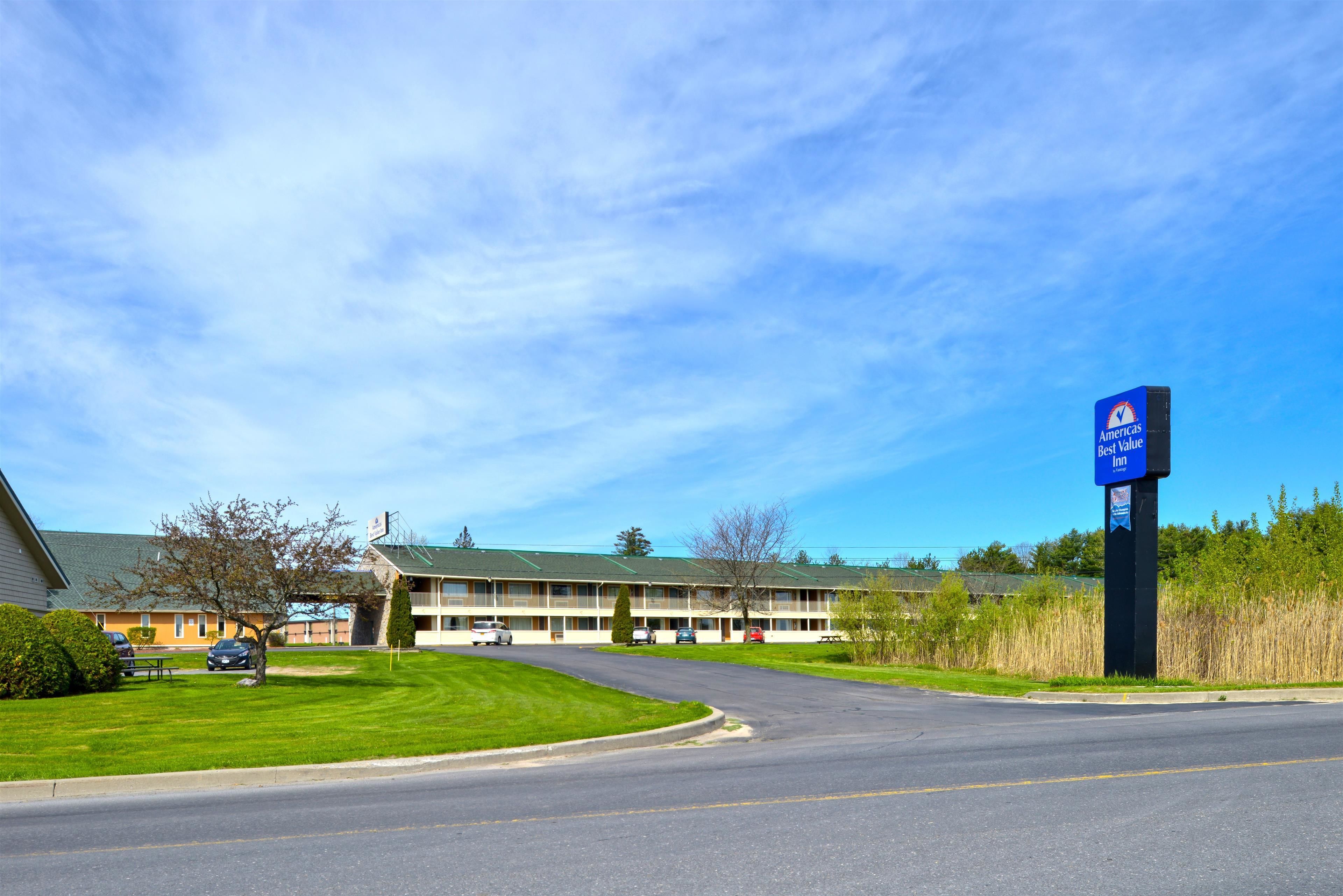 Un motel con césped verde, coches aparcados y un cielo azul despejado.