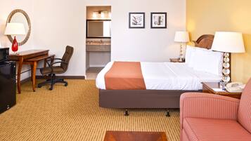 Una habitación de hotel con una cama, un escritorio con una silla, un sofá, una mesita de noche con una lámpara, un teléfono y un espejo.