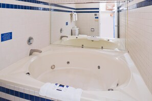 A bathroom with a large bathtub, a toilet, and a sink. There is a sign on the wall and a towel hanging on the wall.