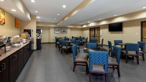 Um espaço de refeições de hotel com várias mesas e cadeiras, um balcão de buffet e uma televisão na parede.