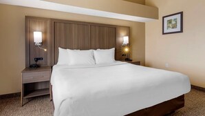 Quarto de hotel com uma cama grande, duas mesas de cabeceira com luminárias, uma mesinha de apoio e um quadro na parede.