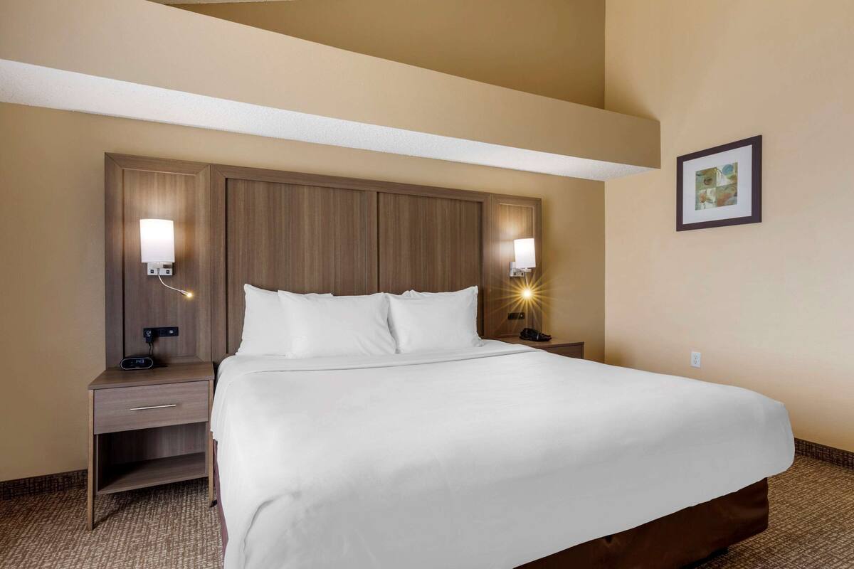 A hotel room with a large bed, two bedside tables with lamps, a nightstand, and a framed picture on the wall.