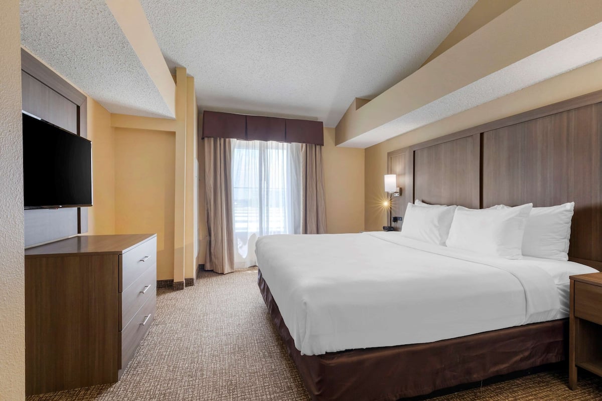 A hotel room with a large bed, a flat-screen TV, a wooden dresser, and a window with curtains.