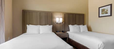 A hotel room with two single beds, a nightstand with a lamp, and a framed picture on the wall.