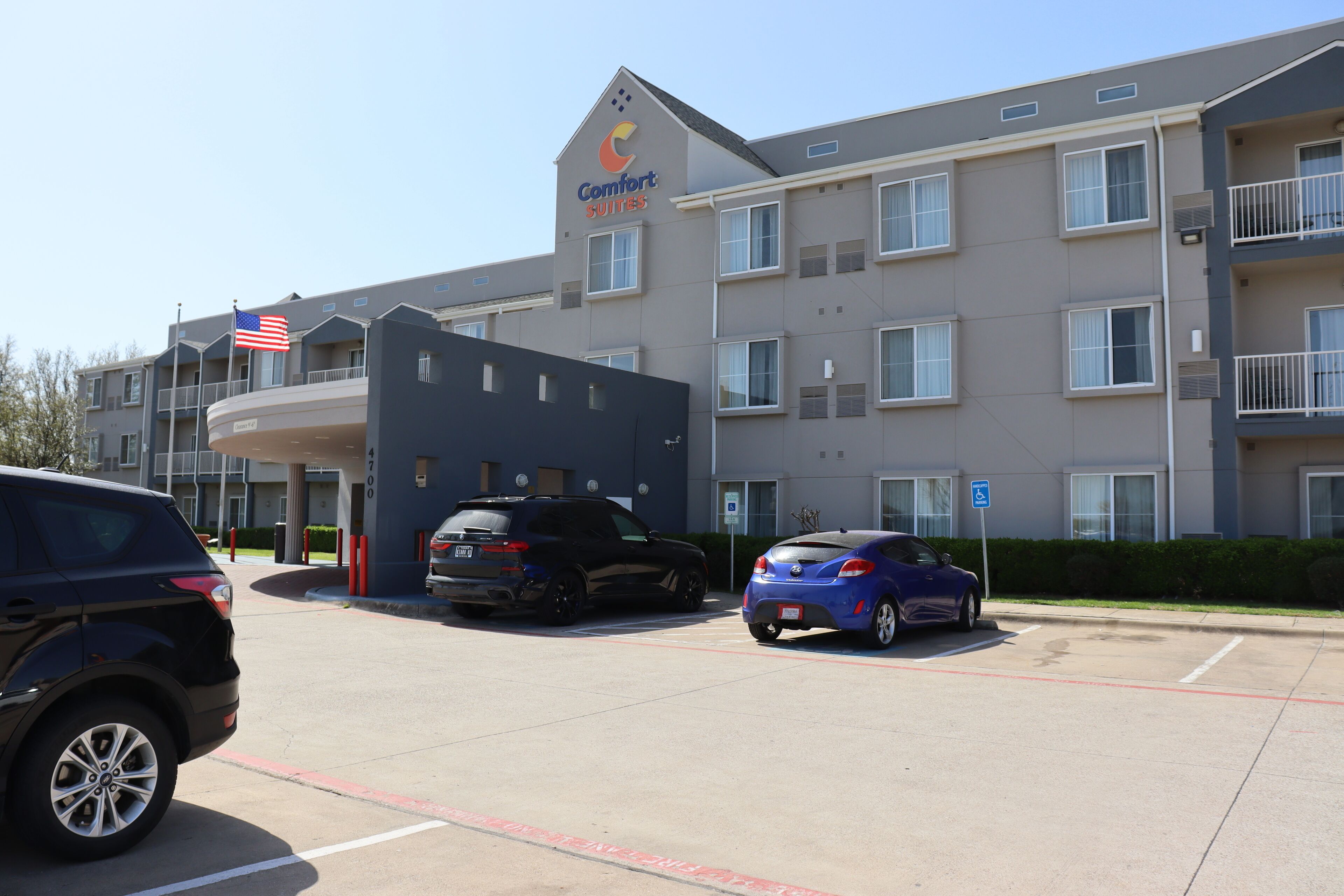 Ett hotell med modern design, med en tydlig skylt som visar att det är ett "Comfort Suites"-hotell. Det finns flera synliga parkeringsplatser, och en amerikansk flagga vajar på byggnaden.