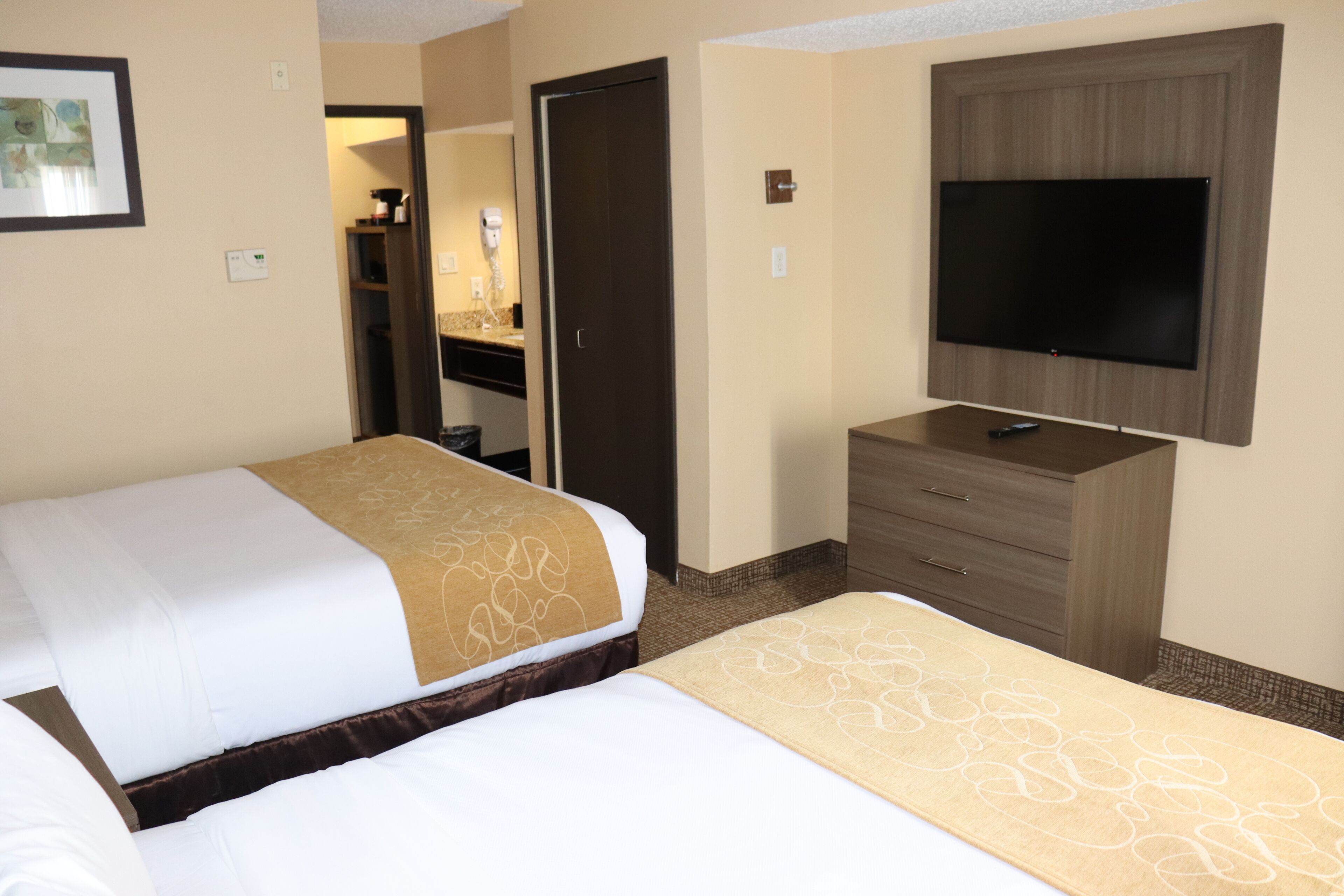 Ett hotellrum med två sängar, en tv, en byrå och ett badrum som syns genom en öppen dörr.