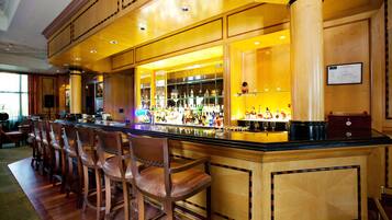 A bar area with wooden bar stools, a polished bar counter, and a variety of bottles and glasses.