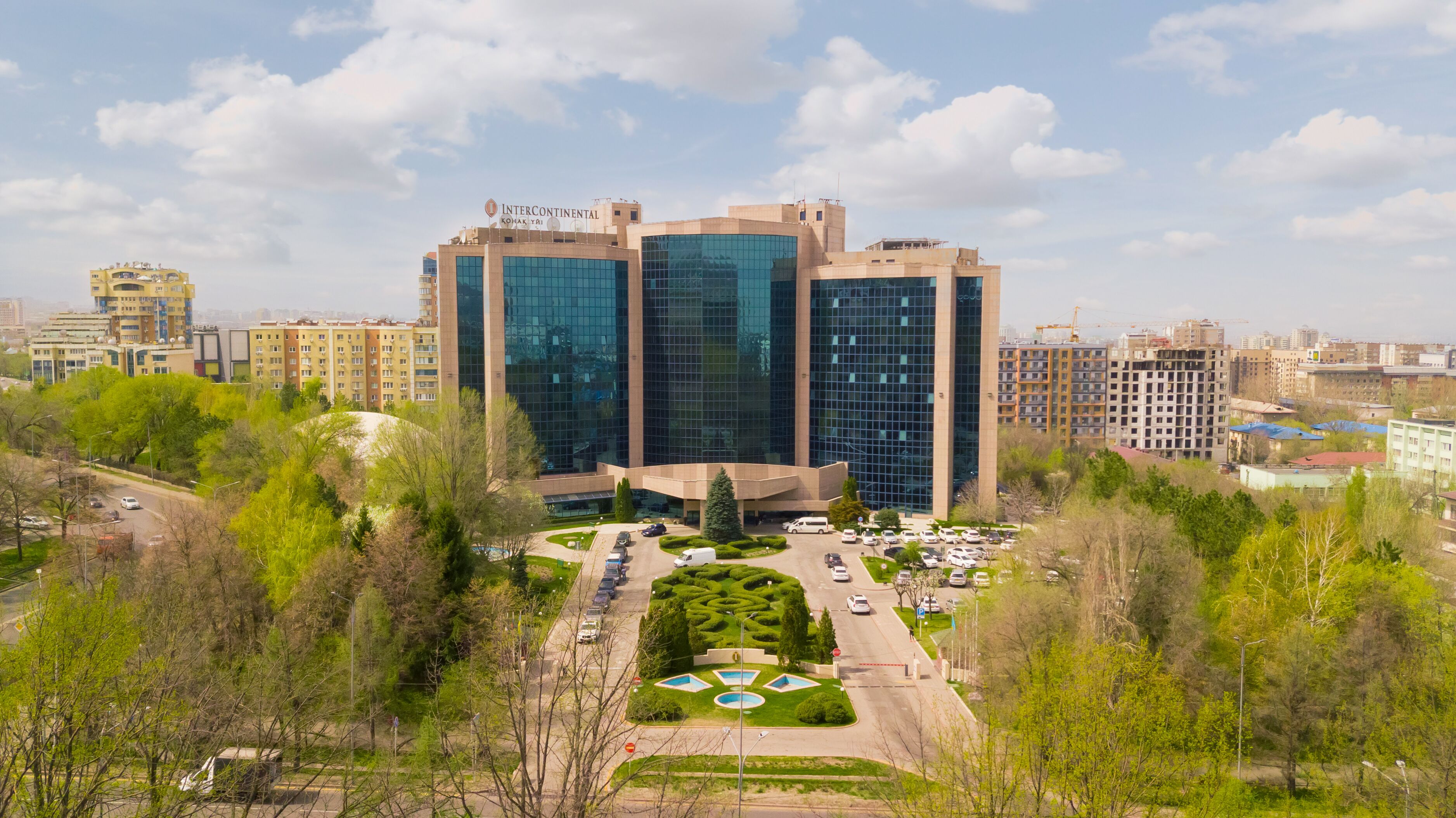 Un edificio moderno con fachada de vidrio, rodeado de vegetación y un área de estacionamiento.