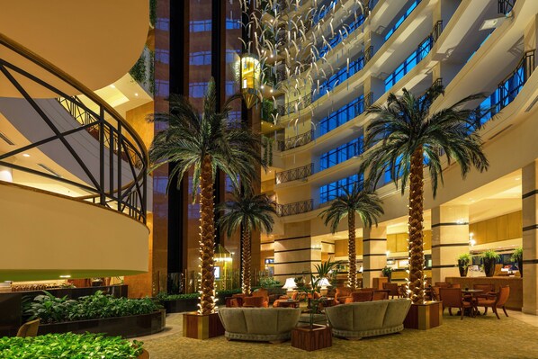 A multi-level hotel lobby with a grand staircase, palm trees, and a seating area.