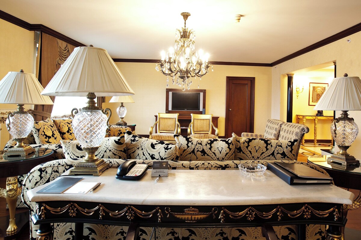 A luxurious living room with a large sofa, ornate lamps, a chandelier, and a television.