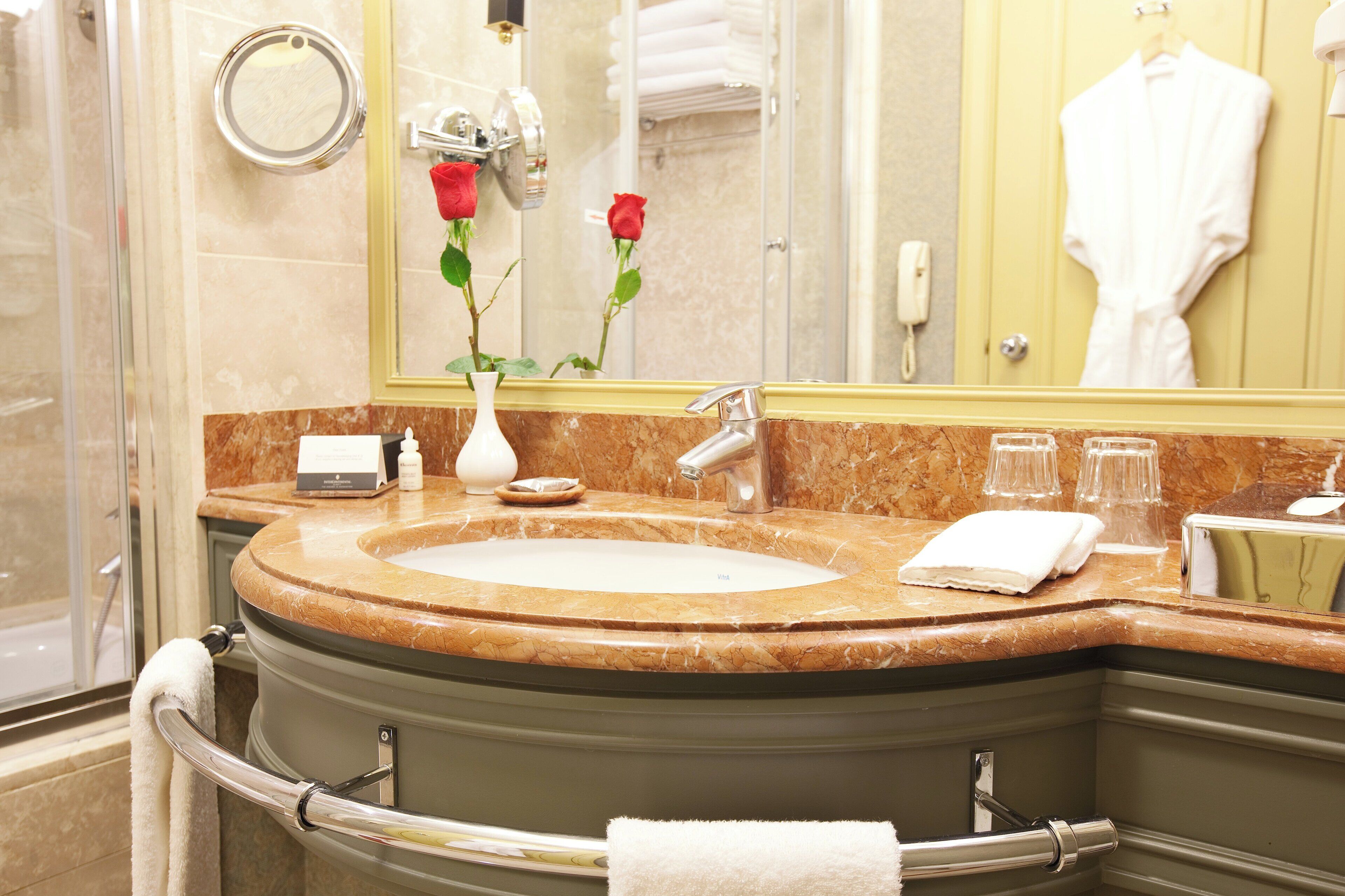 A bathroom with a marble sink, a mirror, a vase with roses, and a towel rack.