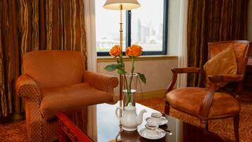 Hotelkamer met zithoek, bestaande uit twee oranje fauteuils, een tafel met theepot, kopjes en een vaas met rozen.