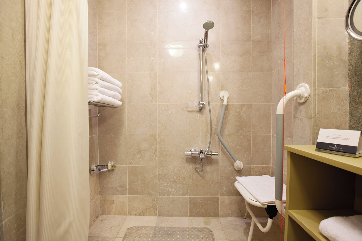 A bathroom with a shower, a towel rack, and a shelf with toiletries.