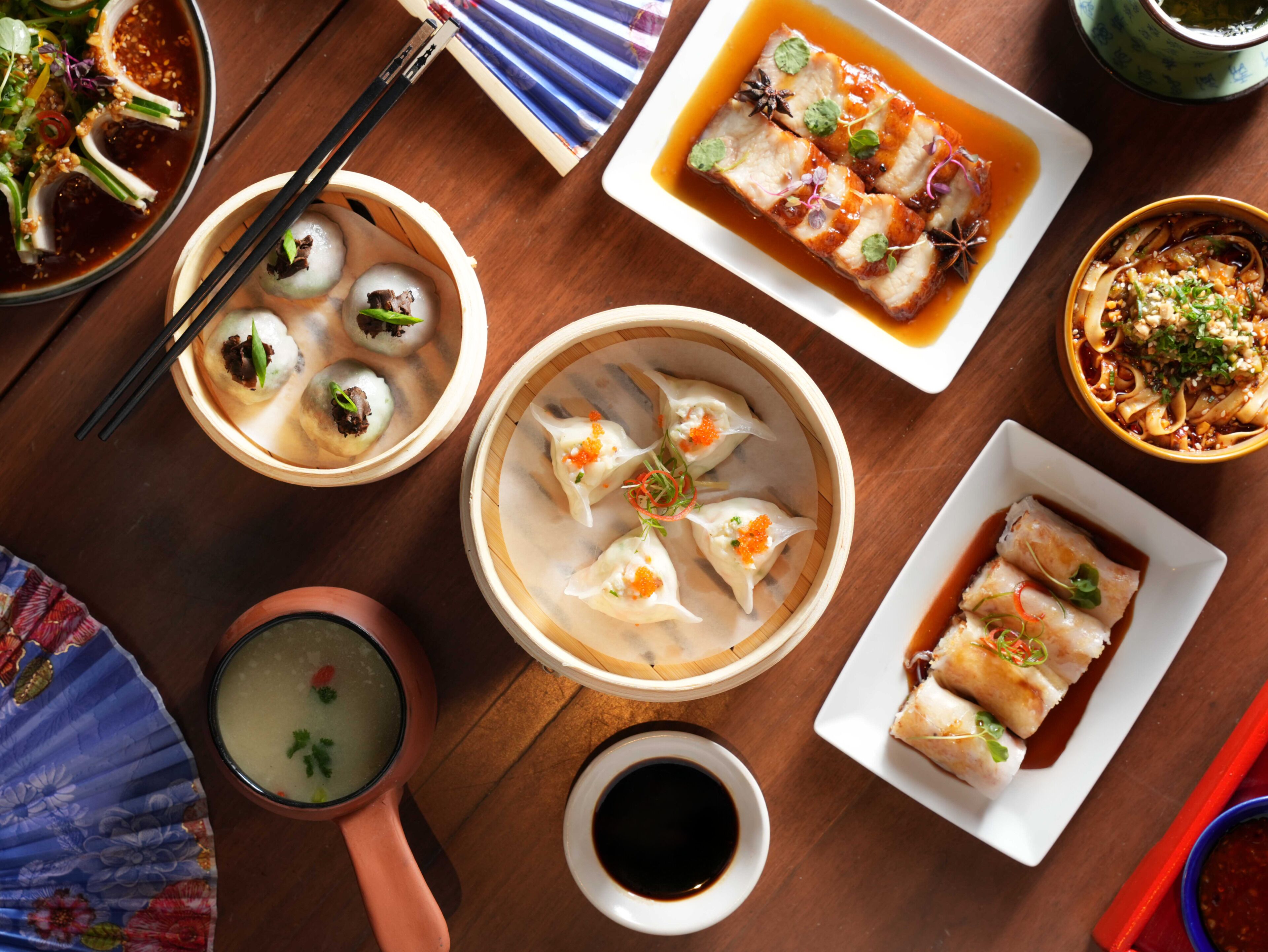 Una variedad de platos asiáticos, como dumplings, sopa y pescado, sobre una mesa de madera.
