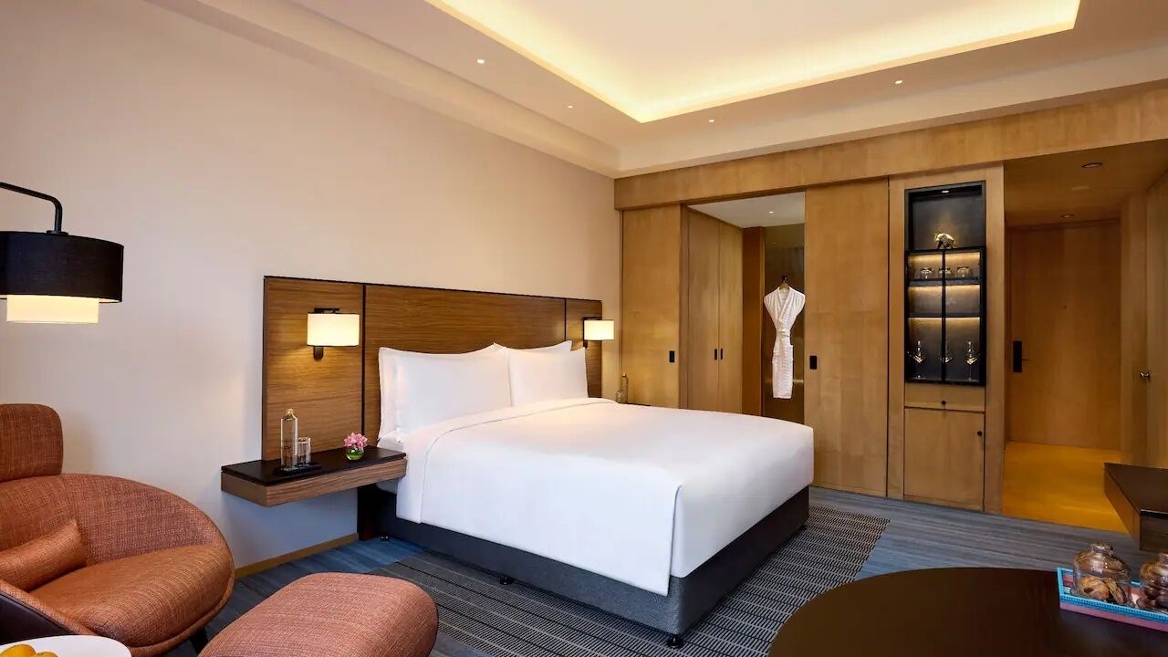 Una habitación de hotel con cama, mesita de noche, lámpara, silla, mesa y armario.