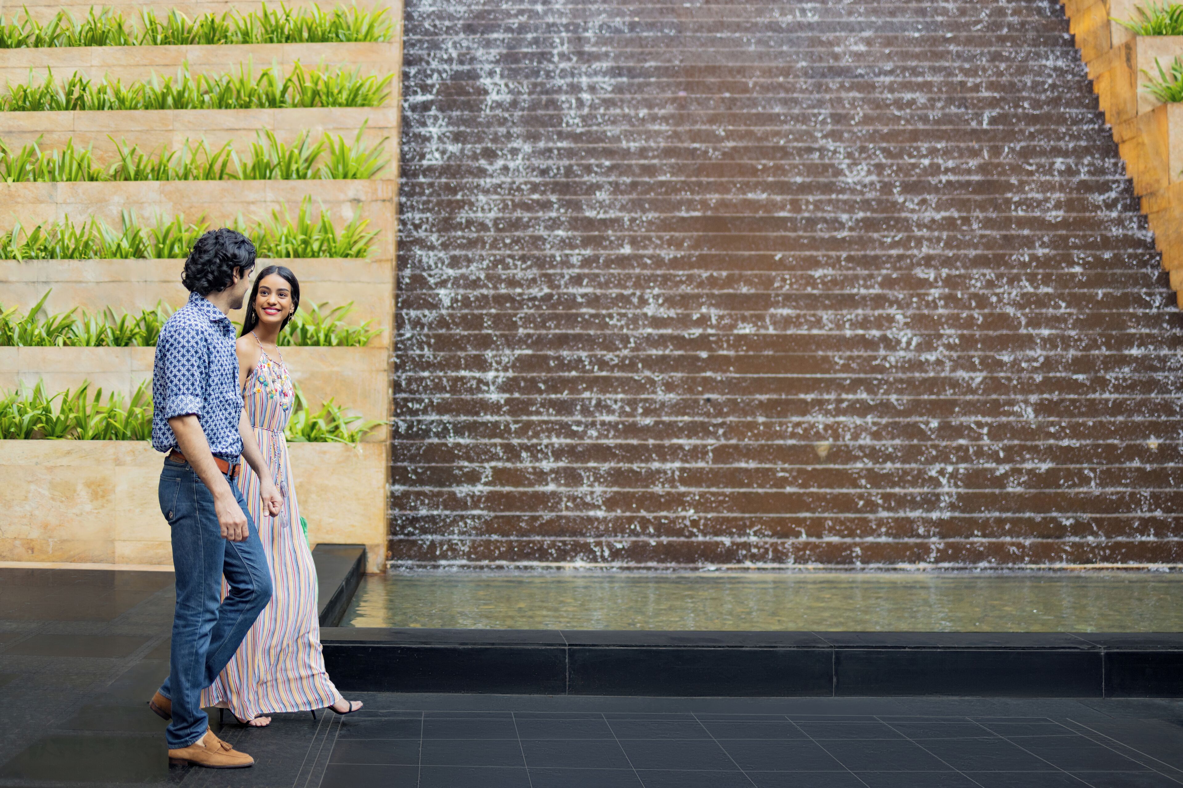 A couple walking past a water feature with steps and greenery.