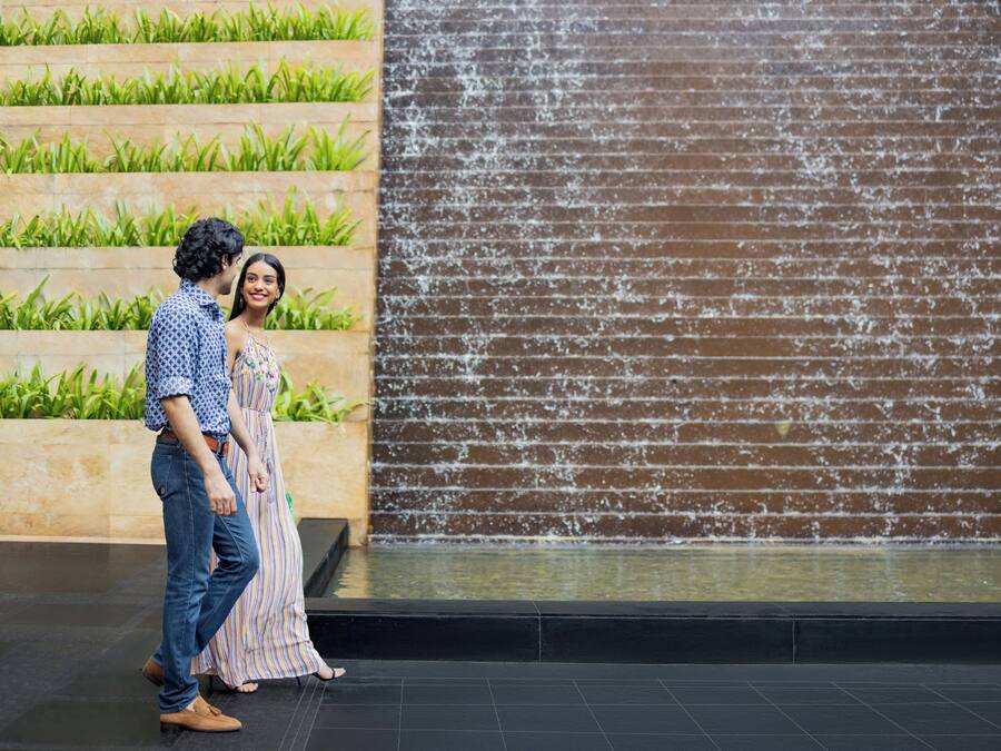 A couple walking past a water feature with steps and greenery.