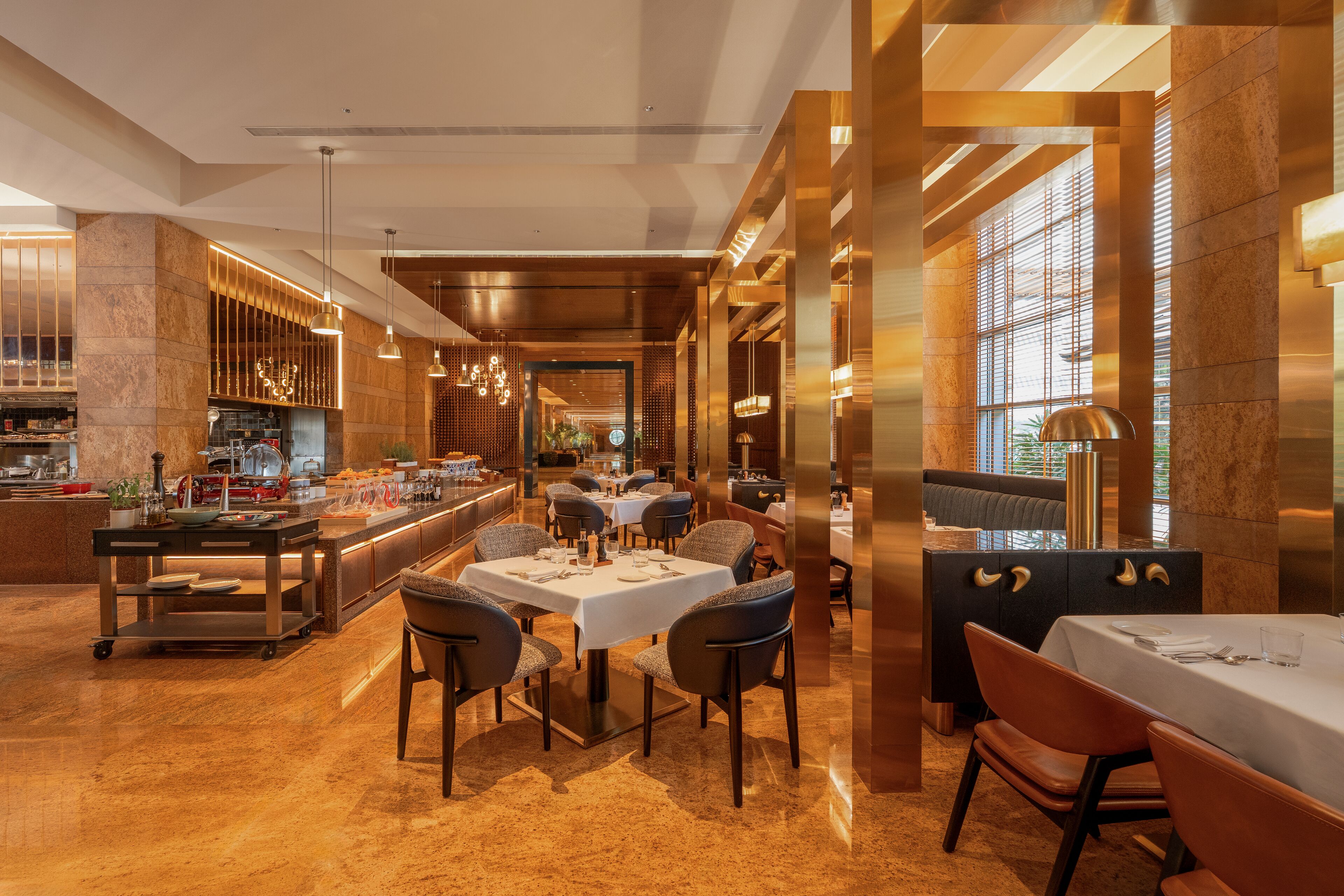 A modern restaurant with a central dining area, a bar, and a kitchen visible in the background.