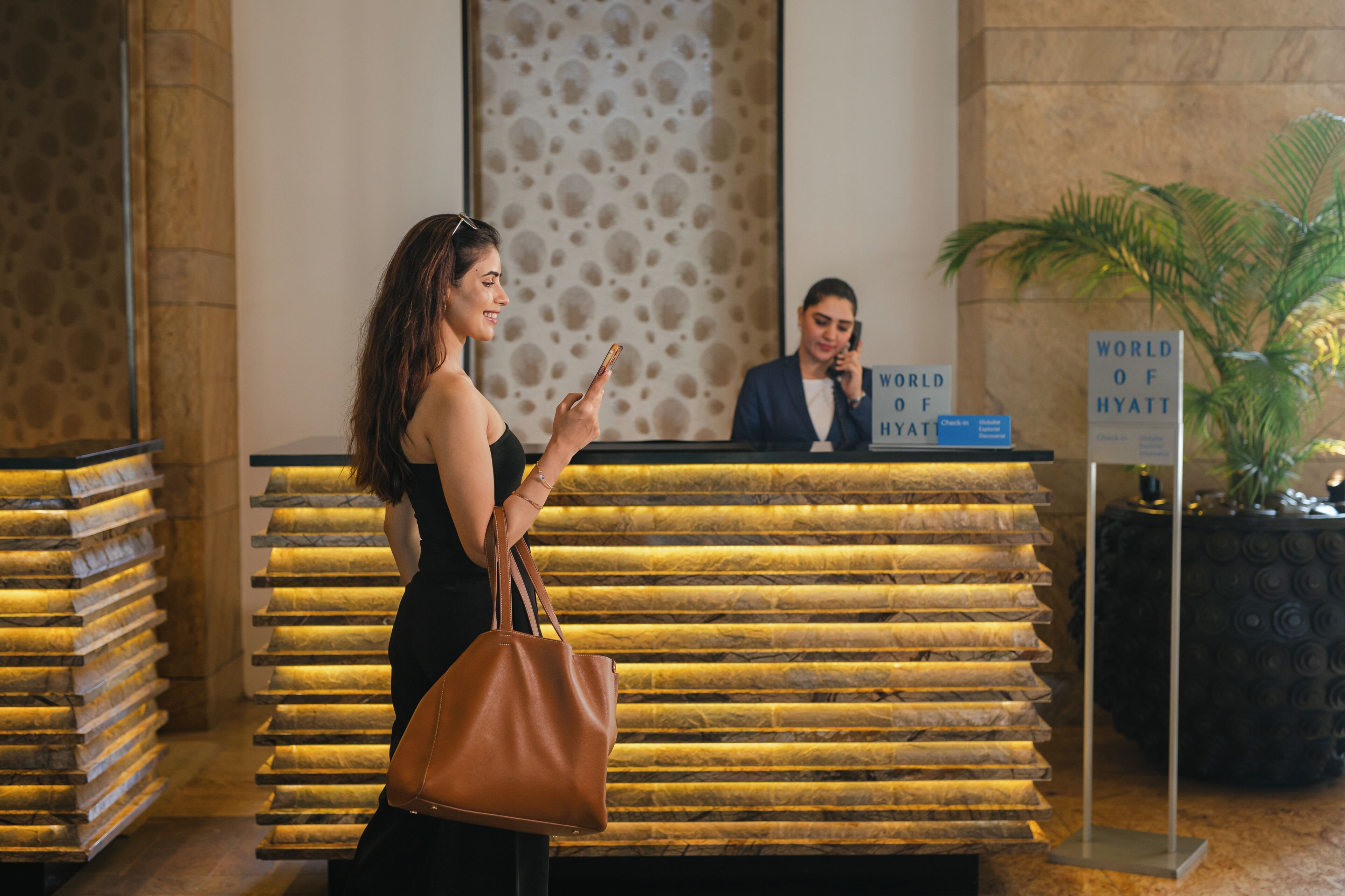 A reception desk with a sign reading 'WORLD OF HYATT,' a woman standing with a handbag, and a receptionist behind the desk.
