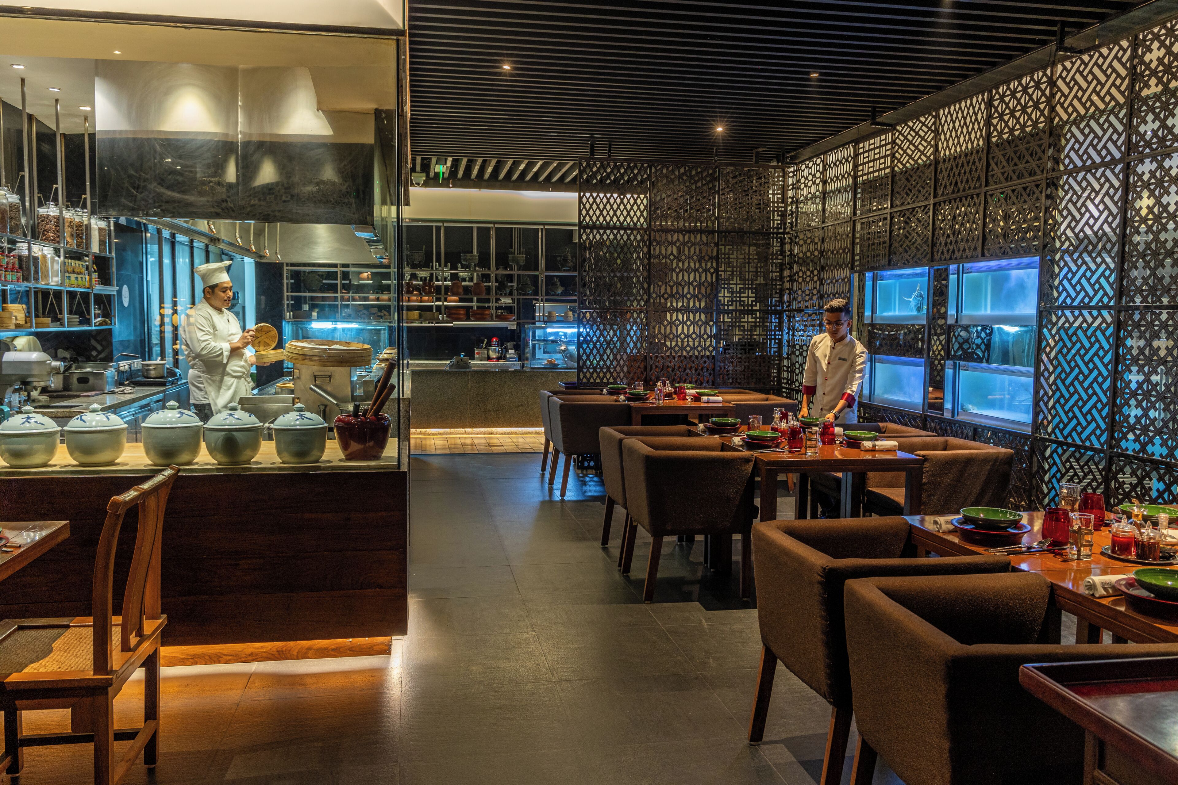 Un interno ristorante moderno con uno chef che prepara cibo, tavoli di legno e una parete decorata.