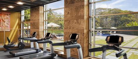 A gym with treadmills, exercise bikes, and a large window offering a view of a green outdoor area.