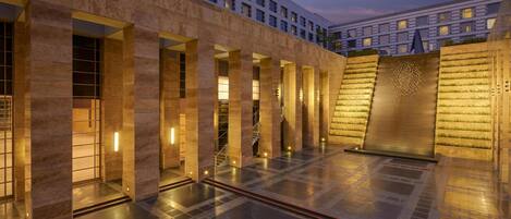 A modern building with a courtyard, featuring a series of columns, a staircase, and a wall with a geometric pattern.
